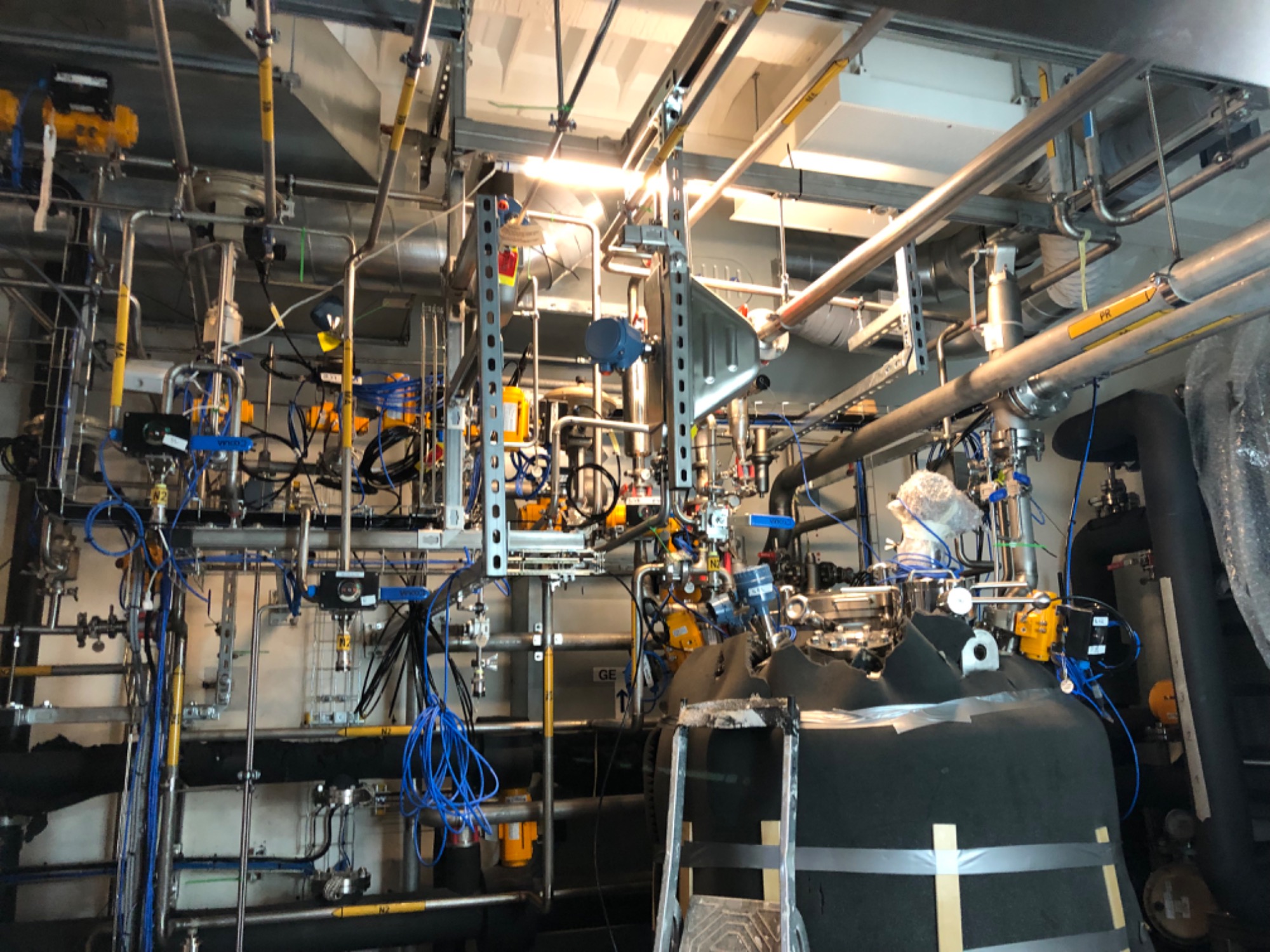 Kompleksowa instalacja przemysłowa z rurami, zaworami i przewodami, widoczne elementy konstrukcji stalowej i zbiornik izolowany termicznie.