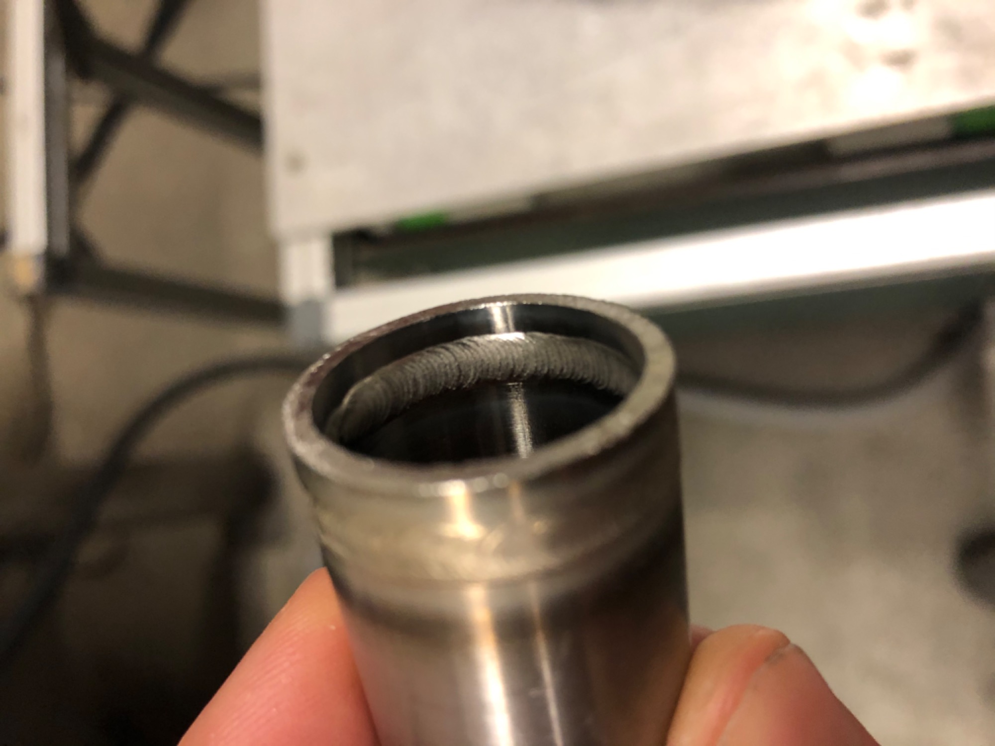 Detal wewnętrznego spawu wewnątrz metalowej rury, trzymanej w palcach, widoczne ślady po spawaniu
