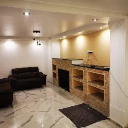 Wykończone wnętrze salonu z marmurową podłogą, brązową skórzaną sofą, ścianą akcentową z kamienia dekoracyjnego i czarnym blatem, oświetleniem sufitowym i wiszącą lampą z trzema żarówkami.