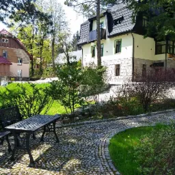 Pensjonat z ogrodem: kamienny chodnik, stolik z krzesłami, trawnik, budynek z kamienną elewacją i czarnym dachem.