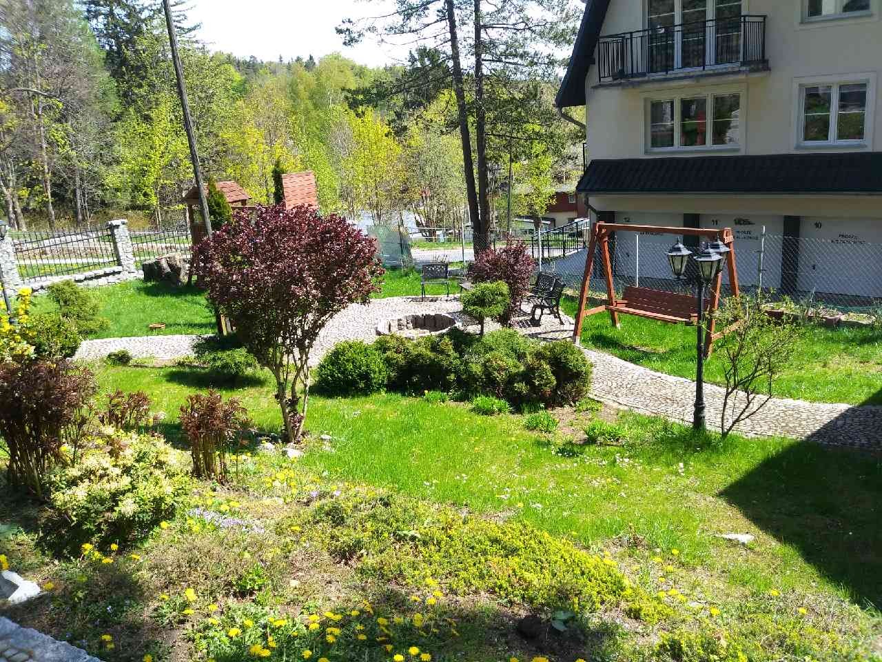 Urokliwy ogród pensjonatu z drewnianą huśtawką, kamienną ścieżką i widokiem na las w tle.