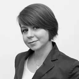 Portret kobiety w marynarce, czarno-białe zdjęcie, subtelny uśmiech, krótka fryzura, wisiorek na szyi.