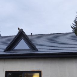 PPHU Czesław Gołębiewski - Szary dach z dachówki ceramicznej z trójkątnym oknem dachowym, widoczne elementy konstrukcji drewnianej domu w trakcie budowy.