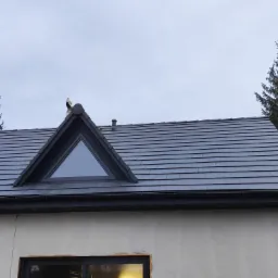 Szary dach z dachówki ceramicznej z trójkątnym oknem dachowym, widoczne elementy konstrukcji drewnianej domu w trakcie budowy.