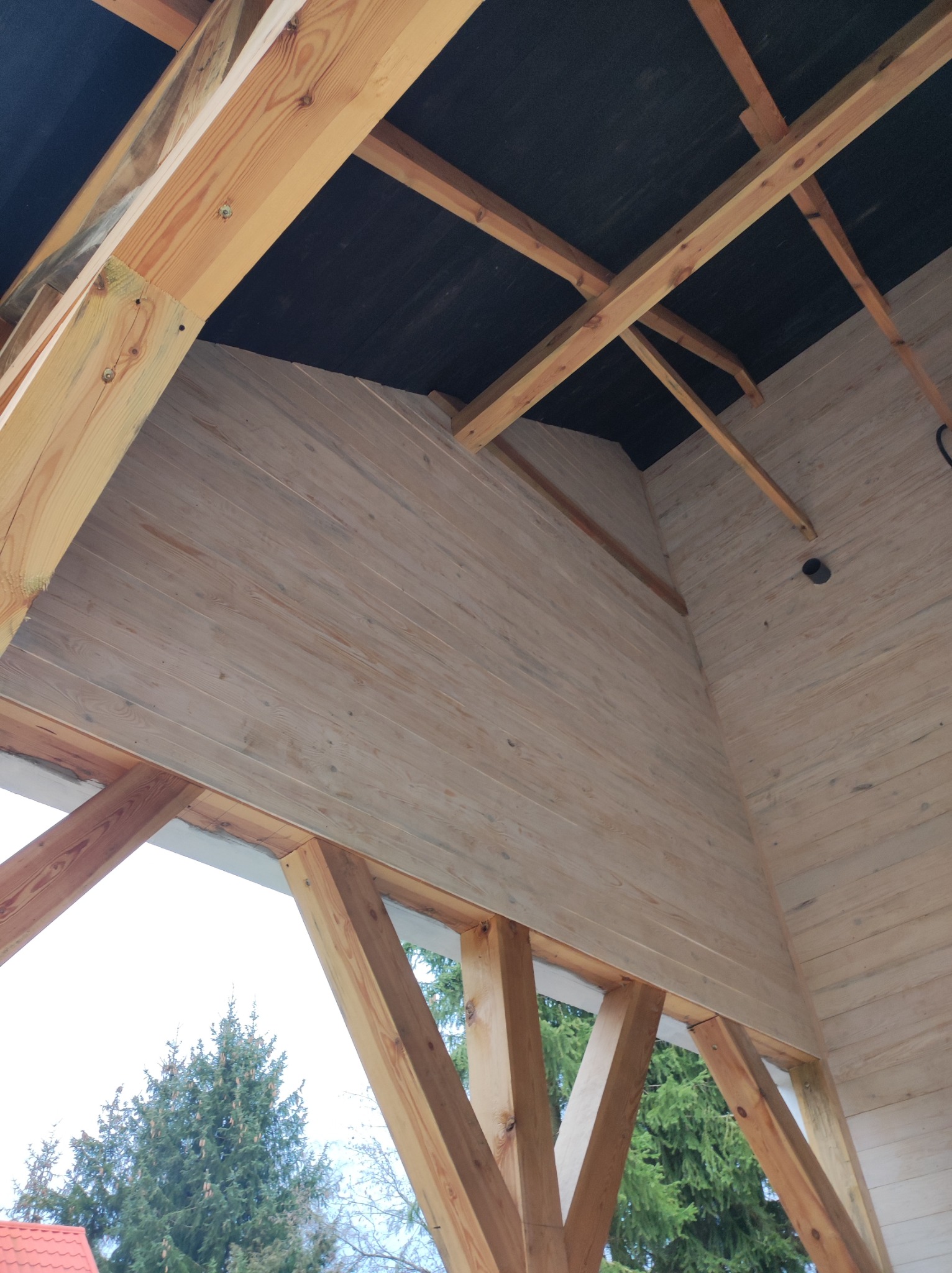 Wnętrze w surowym stanie domu szkieletowego z widoczną konstrukcją drewnianą, deskowaniem ścian i czarną membraną dachową.