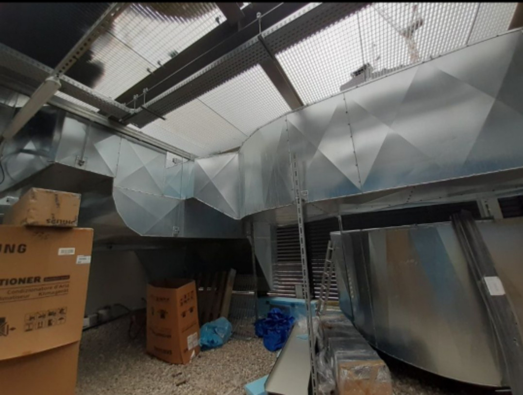 Skomplikowany system kanałów wentylacyjnych z blachy ocynkowanej pod sufitem, widoczne skrzynki kartonowe i elementy montażowe.