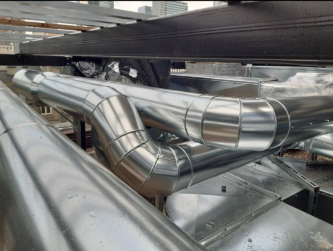 System rur wentylacyjnych z metalu na dachu budynku, widoczne elementy mocujące i połączenia segmentowe.