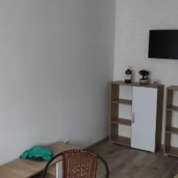 Jasne wnętrze pokoju po remoncie z białymi ścianami, drewnianą podłogą, meblami i wiklinowym krzesłem na pierwszym planie.