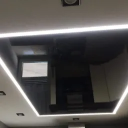 Czarny sufit napinany z wbudowanym oświetleniem LED w kształcie kwadratu, widoczne punktowe lampy halogenowe i odbicie wnętrza pomieszczenia.