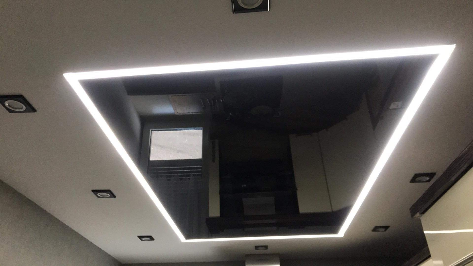 Czarny sufit napinany z wbudowanym oświetleniem LED w kształcie kwadratu, widoczne punktowe lampy halogenowe i odbicie wnętrza pomieszczenia.