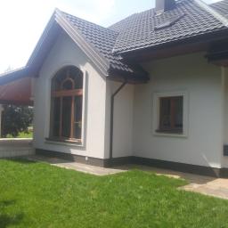 Okna Ola-sprzedaż, montaż drzwi, okien i bram garażowych - Fragment elewacji domu z oknem łukowym i mniejszym oknem prostokątnym, ciemna dachówka, świeżo skoszony trawnik.