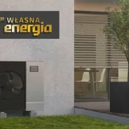 Zewnętrzna jednostka pompy ciepła Mitsubishi Ecodan zamontowana przy nowoczesnym domu z logo 'Własna Energia' na ścianie, widok na taras z meblami ogrodowymi i zachodzące słońce w tle.