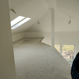Krzysztof - Poddasze w trakcie wykańczania, widoczne okna dachowe, niedokończona podłoga, przygotowane kable elektryczne wystające z sufitu, ściany pomalowane na biało.