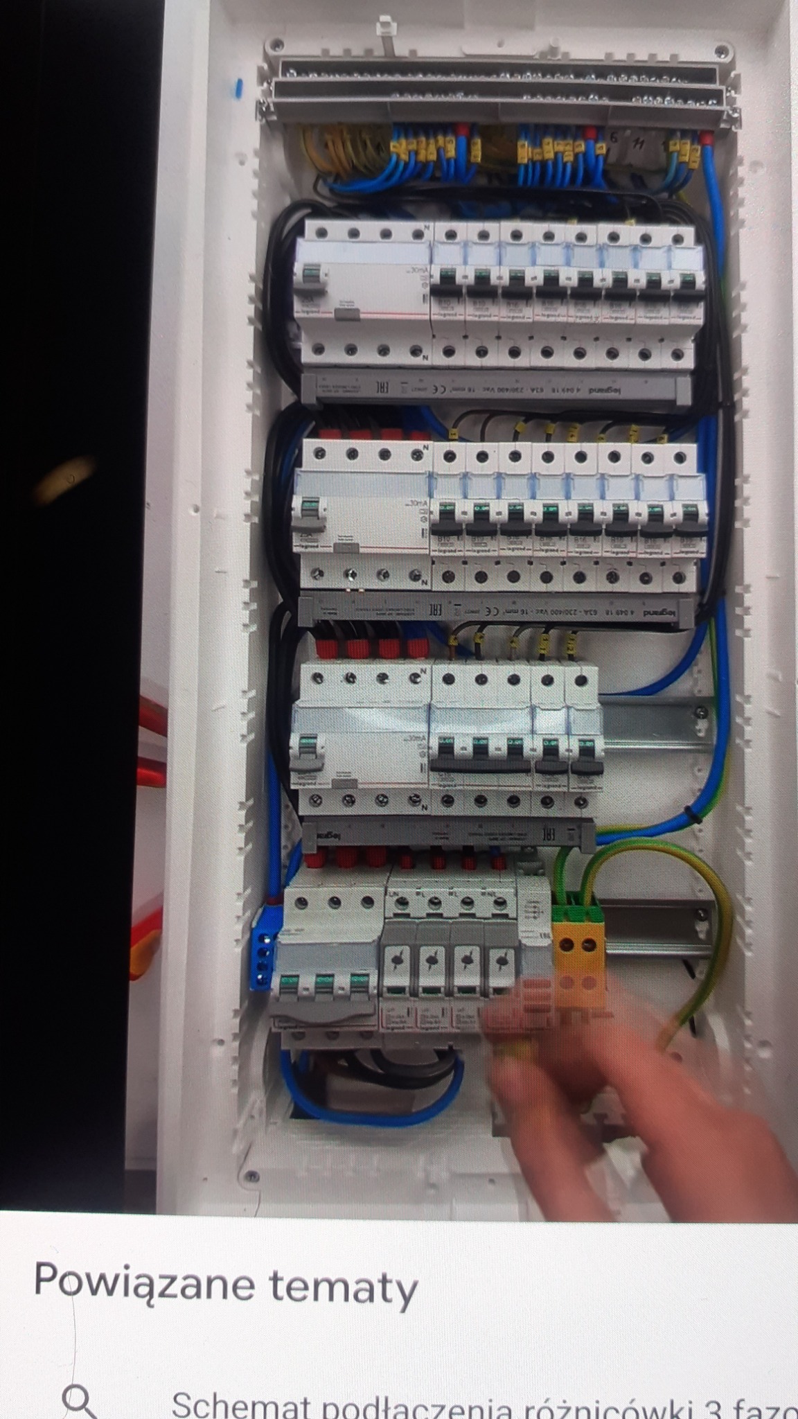 Rozdzielnica elektryczna z zamontowanymi bezpiecznikami i okablowaniem, widoczne ręce osoby pracującej przy instalacji.