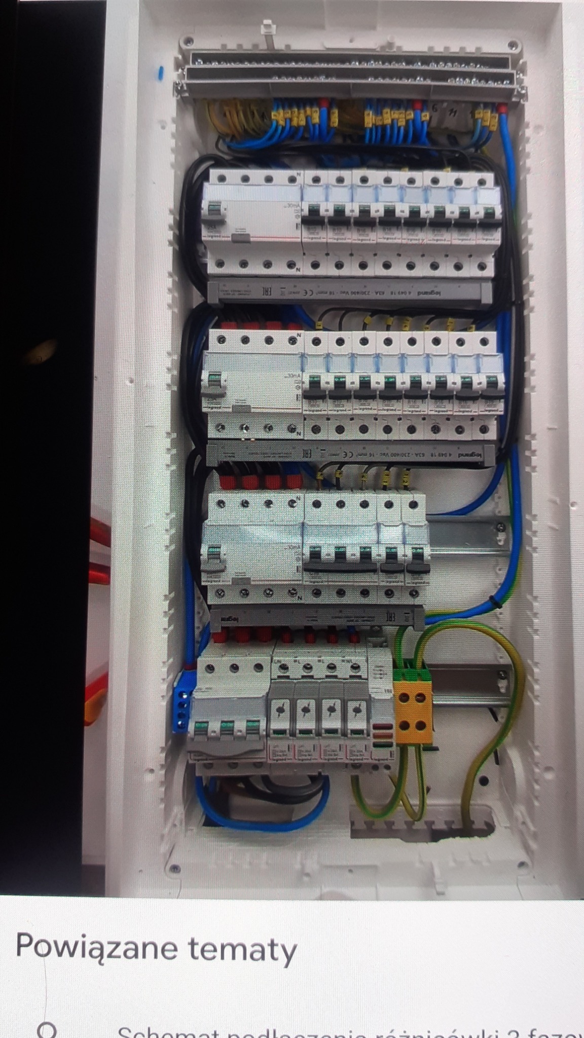 Rozdzielnica elektryczna z bezpiecznikami i okablowaniem, widoczne liczne przewody w różnych kolorach (niebieski, żółto-zielony), listwy zaciskowe i zabezpieczenia firmy Legrand.