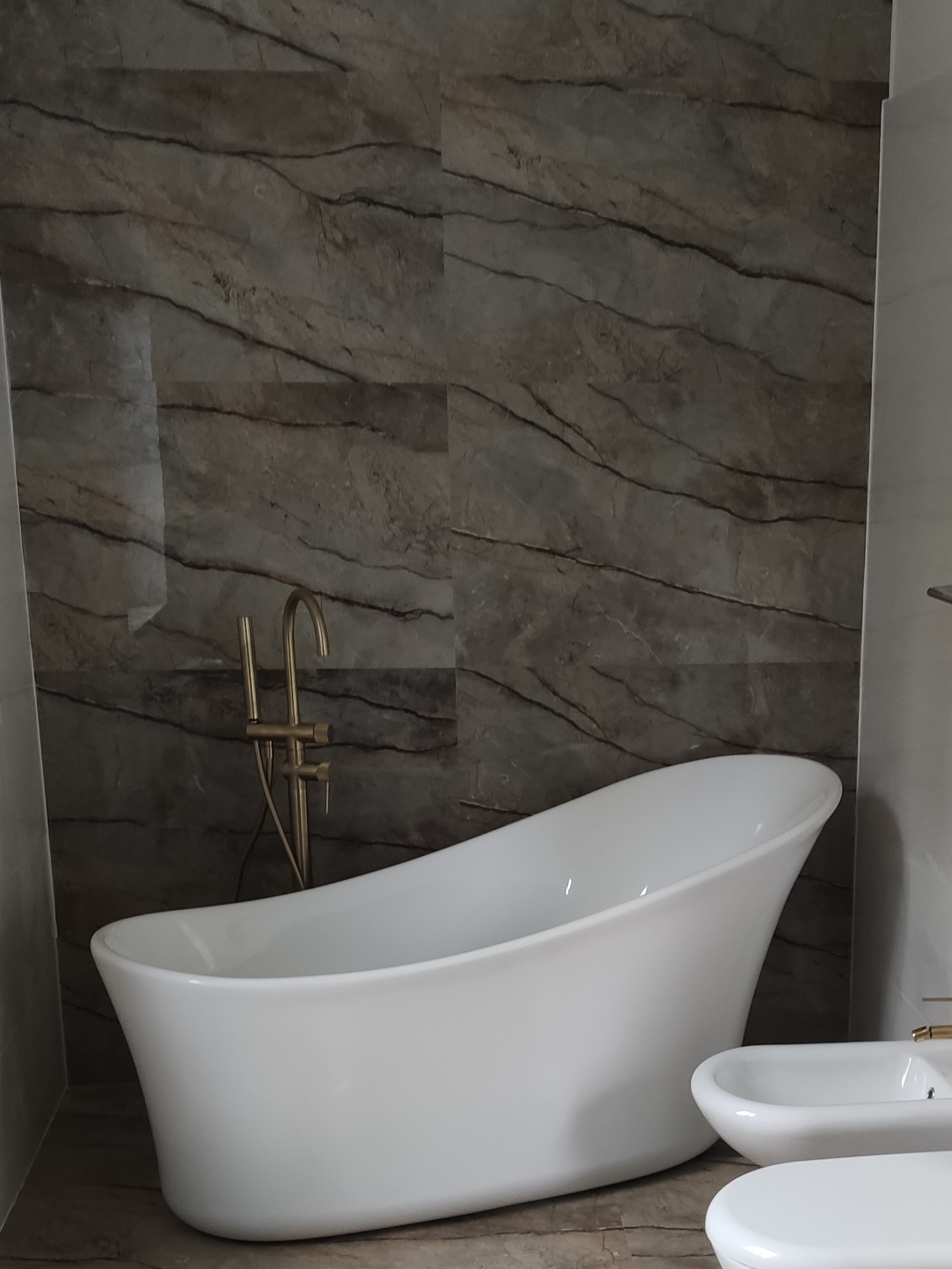 Nowoczesna łazienka z wolnostojącą wanną i marmurową ścianą. Złota bateria dodaje elegancji. Ujęcie z niskiego kąta podkreśla design.