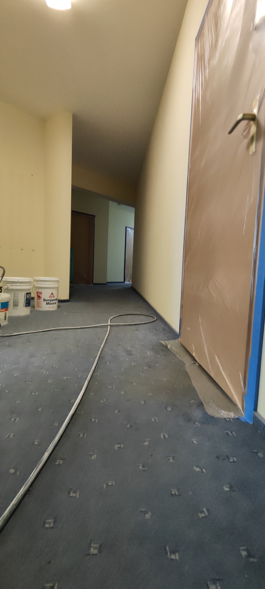 Korytarz w trakcie przygotowań do malowania, widoczne wiaderka z farbą Benjamin Moore, zabezpieczone drzwi i listwy przypodłogowe.
