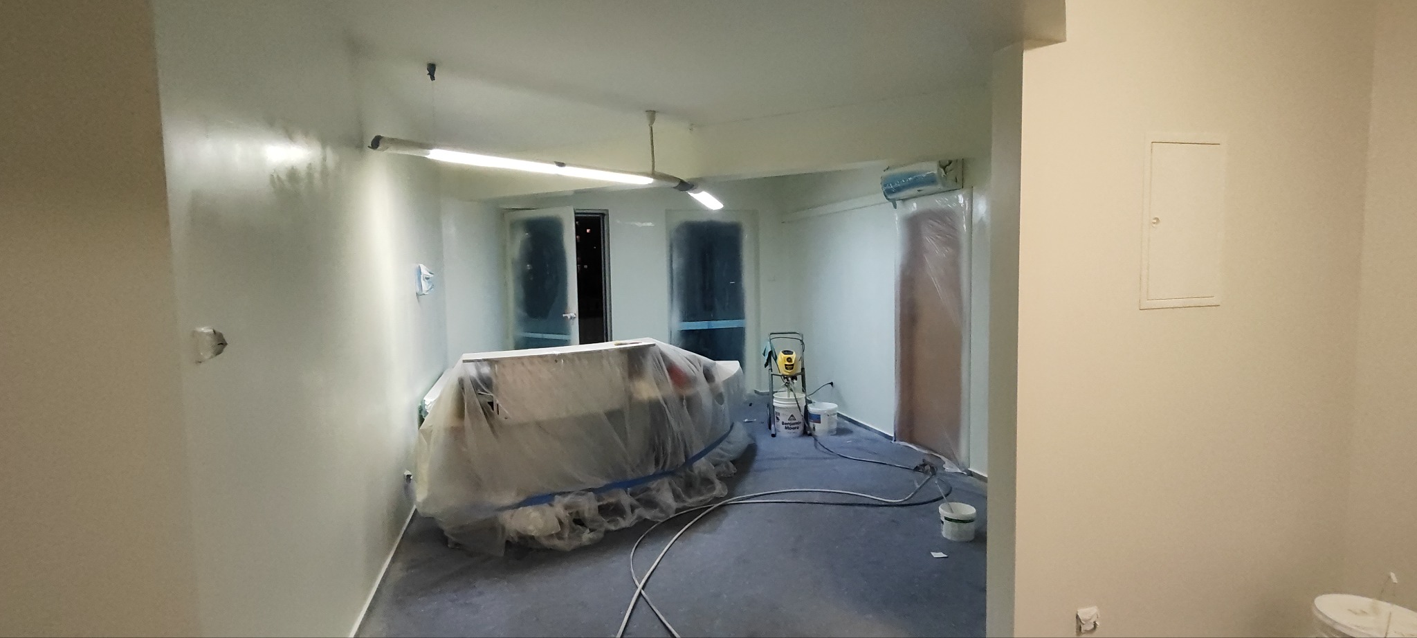 Pokój po malowaniu, meble zabezpieczone folią, widoczny agregat malarski, ściany w jasnym odcieniu, świeżo pomalowane.