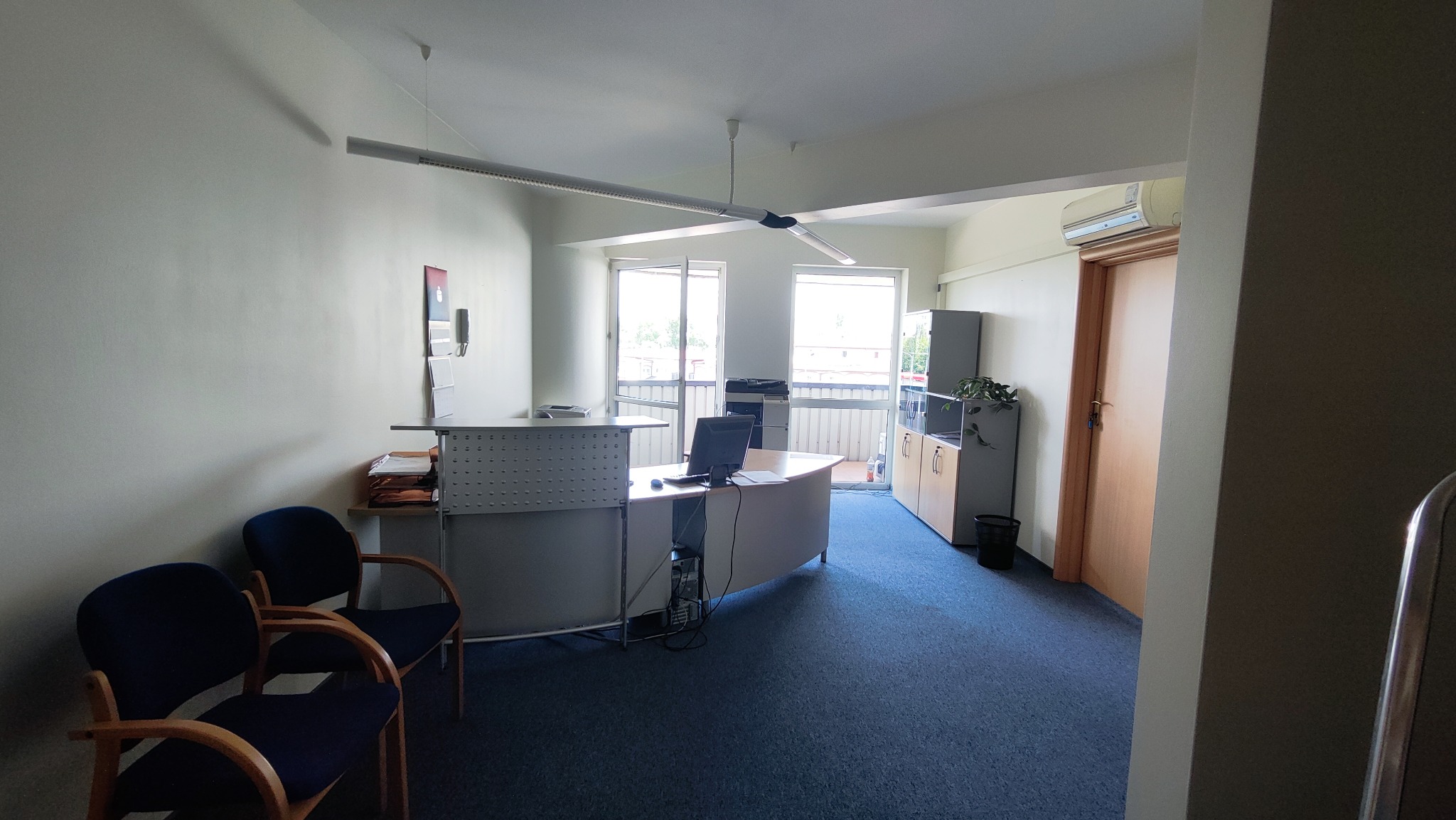 Jasne biuro z recepcją, biurkiem z komputerem, krzesłami dla klientów i klimatyzacją, świeżo po malowaniu ścian na biało.