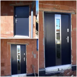 Nowoczesne, antracytowe drzwi wejściowe z przeszkleniem, zamontowane w surowym murze z czerwonej cegły, widoczne ślady zaprawy i instalacji elektrycznej.