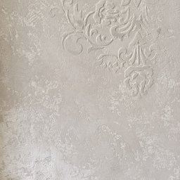 MK-WNĘTRZA - Beżowa ściana z dekoracyjną, wypukłą fakturą w stylu retro. Widoczny fragment podłogi. Neutralna kolorystyka, delikatne wzory.