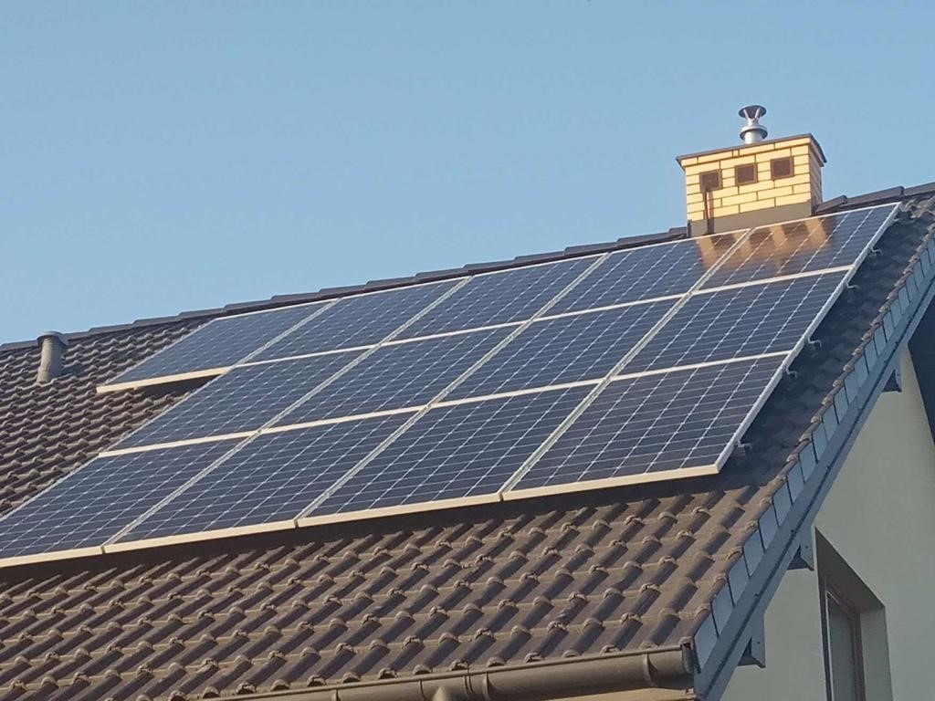 Panele słoneczne na brązowym dachu domu jednorodzinnego z żółtym kominem w słoneczny dzień.