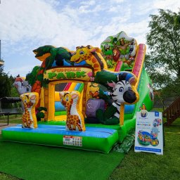 Zbigniew Paprocki - Kolorowy, dmuchany plac zabaw w stylu dżungli z żyrafami, zebrą i zjeżdżalnią, ustawiony na trawie. Obok tablica reklamowa z napisem 'Wynajmij dmuchańca'.