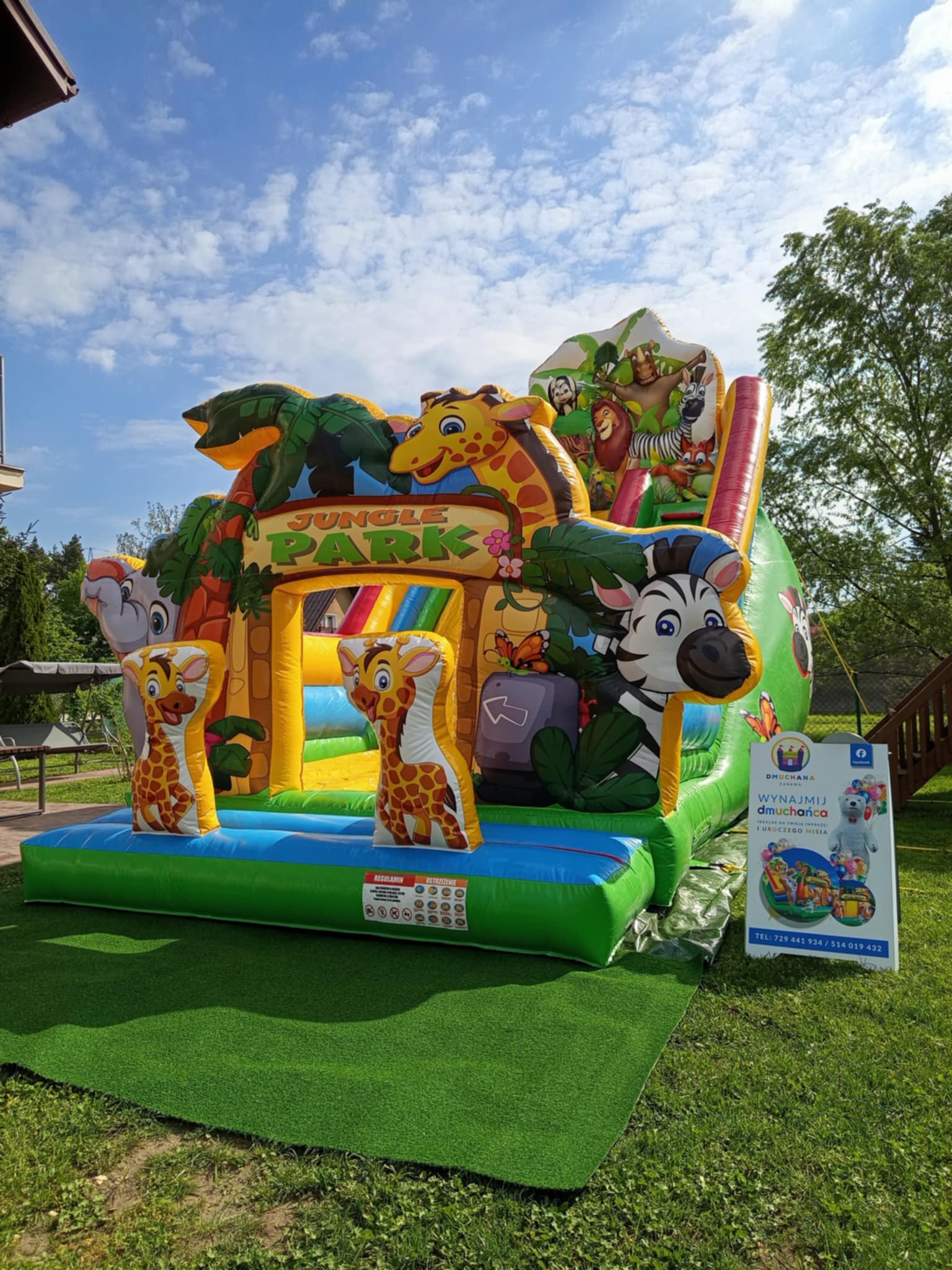Kolorowy, dmuchany plac zabaw 'Jungle Park' z motywami zwierzęcymi, ustawiony na trawie. Widoczny baner reklamowy z ofertą wynajmu dmuchańców.