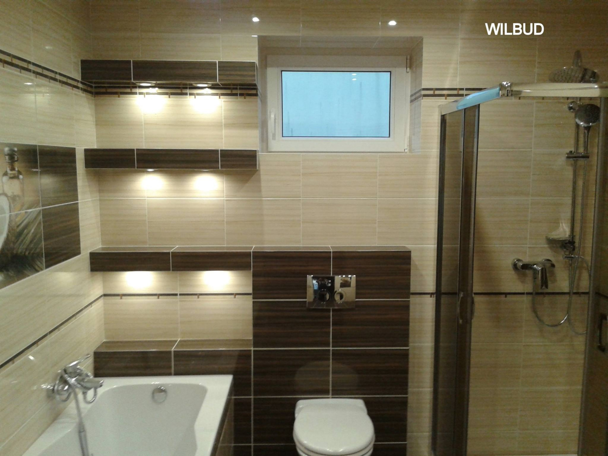 Wykończona łazienka w beżowo-brązowych płytkach z podświetlanymi półkami, kabiną prysznicową i wiszącą toaletą.