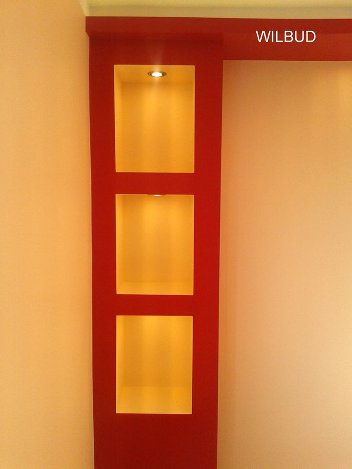 Czerwona zabudowa z trzema podświetlanymi niszami w ścianie, przylegająca do kremowej ściany, z napisem 'WILBUD' w prawym górnym rogu.