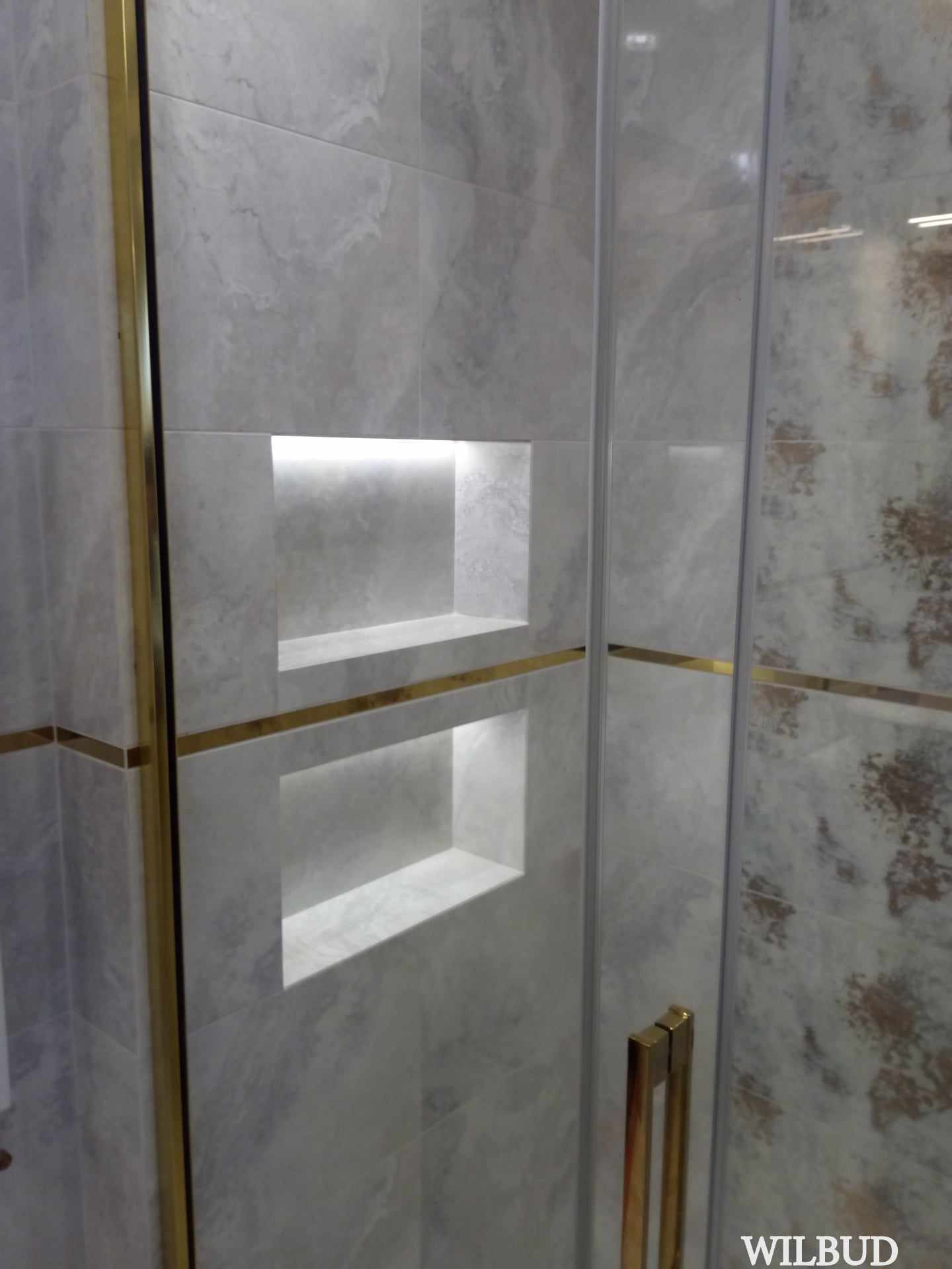Wykończona łazienka z szarymi płytkami imitującymi marmur, wnękami z podświetleniem LED i złotymi akcentami na kabinie prysznicowej.