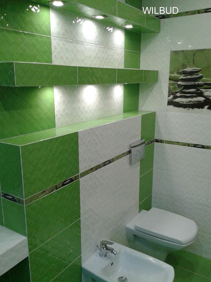 Biało-zielona łazienka z płytkami o wzorze rombów, podświetlane półki, wisząca toaleta i bidet, dekoracja ścienna z motywem zen, logo 'WILBUD' w prawym górnym rogu.