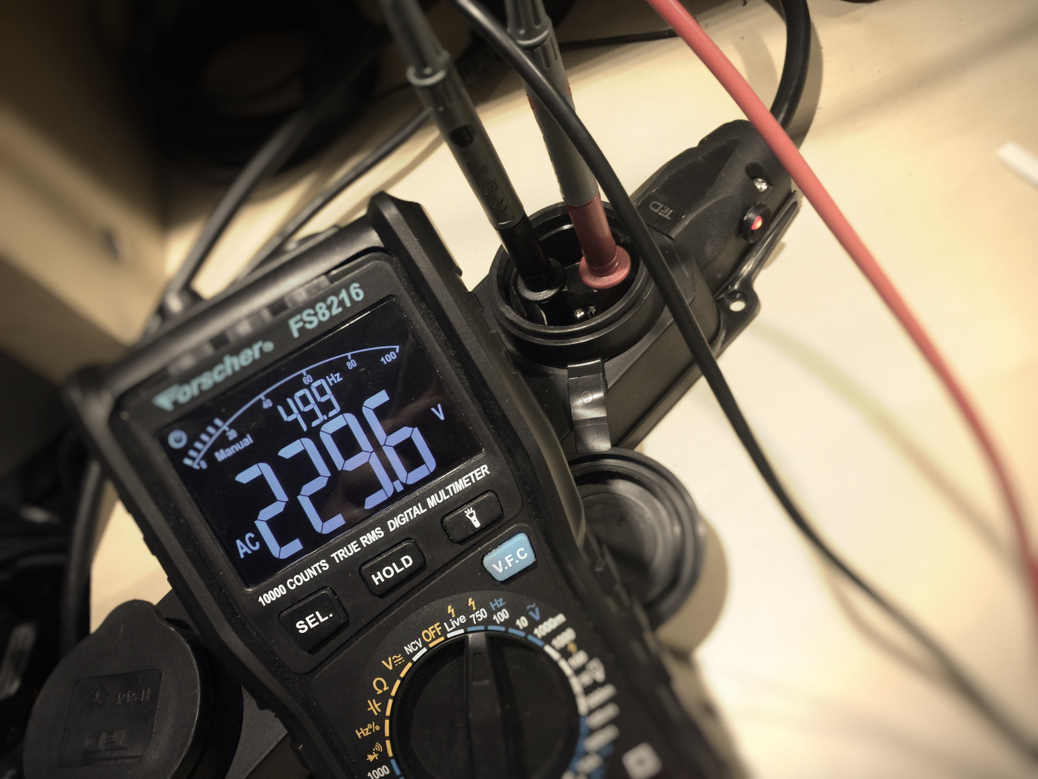 Multimetr cyfrowy Forscher FS8216 z podłączonymi przewodami pomiarowymi, wyświetlający wartość napięcia 229.6V AC.