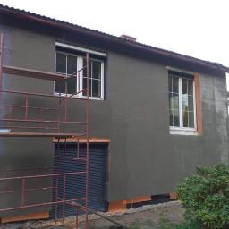 Firma prywatna - Ściana budynku ocieplana styropianem i pokrywana szarym tynkiem, widoczne rusztowanie, okna z białymi ramami i częściowo otynkowana ściana sąsiedniego budynku.