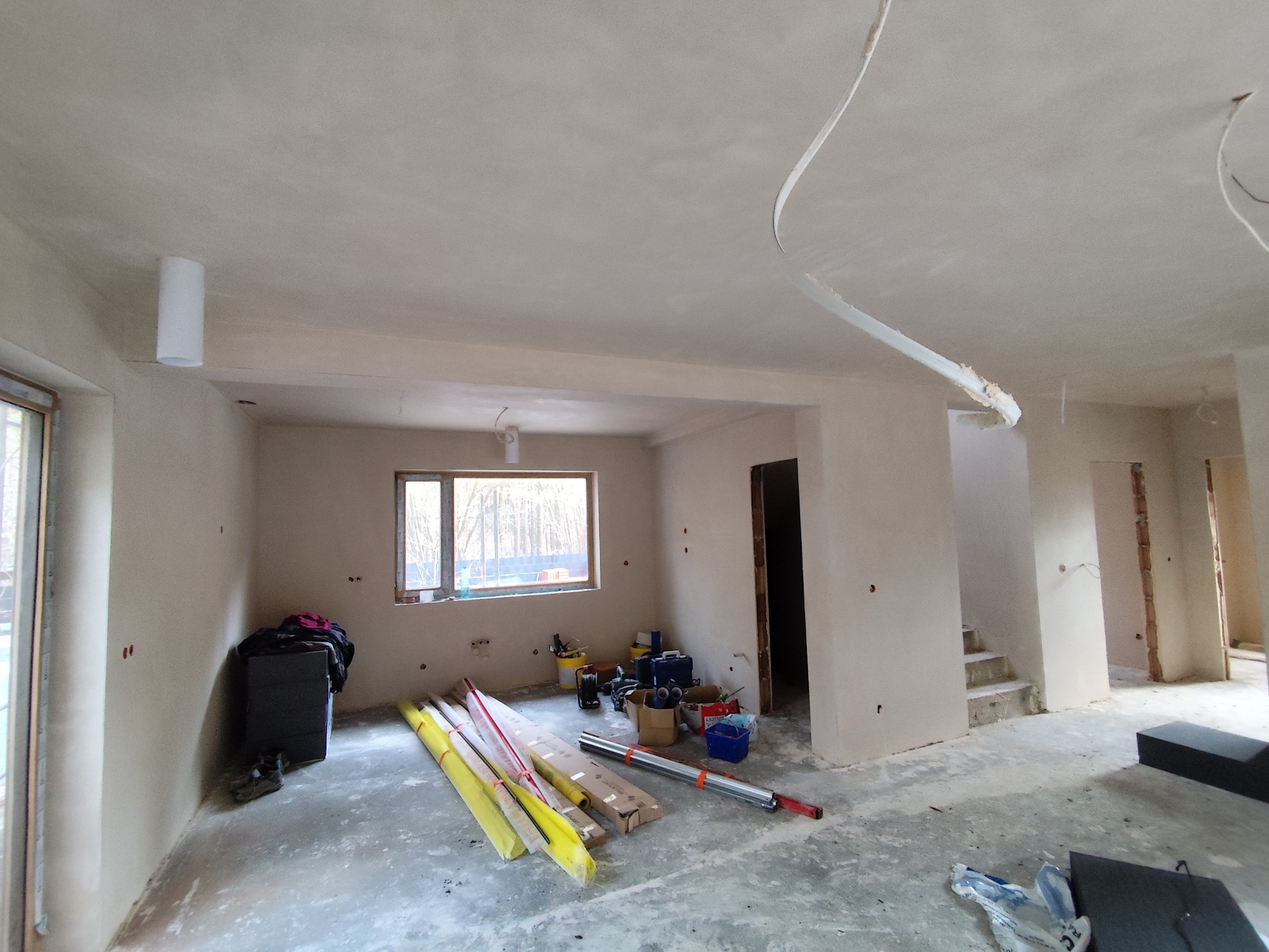 Wnętrze po tynkowaniu maszynowym: gładkie, jasne ściany, widoczne narzędzia i materiały budowlane. Stan surowy, przygotowany do dalszych prac wykończeniowych.