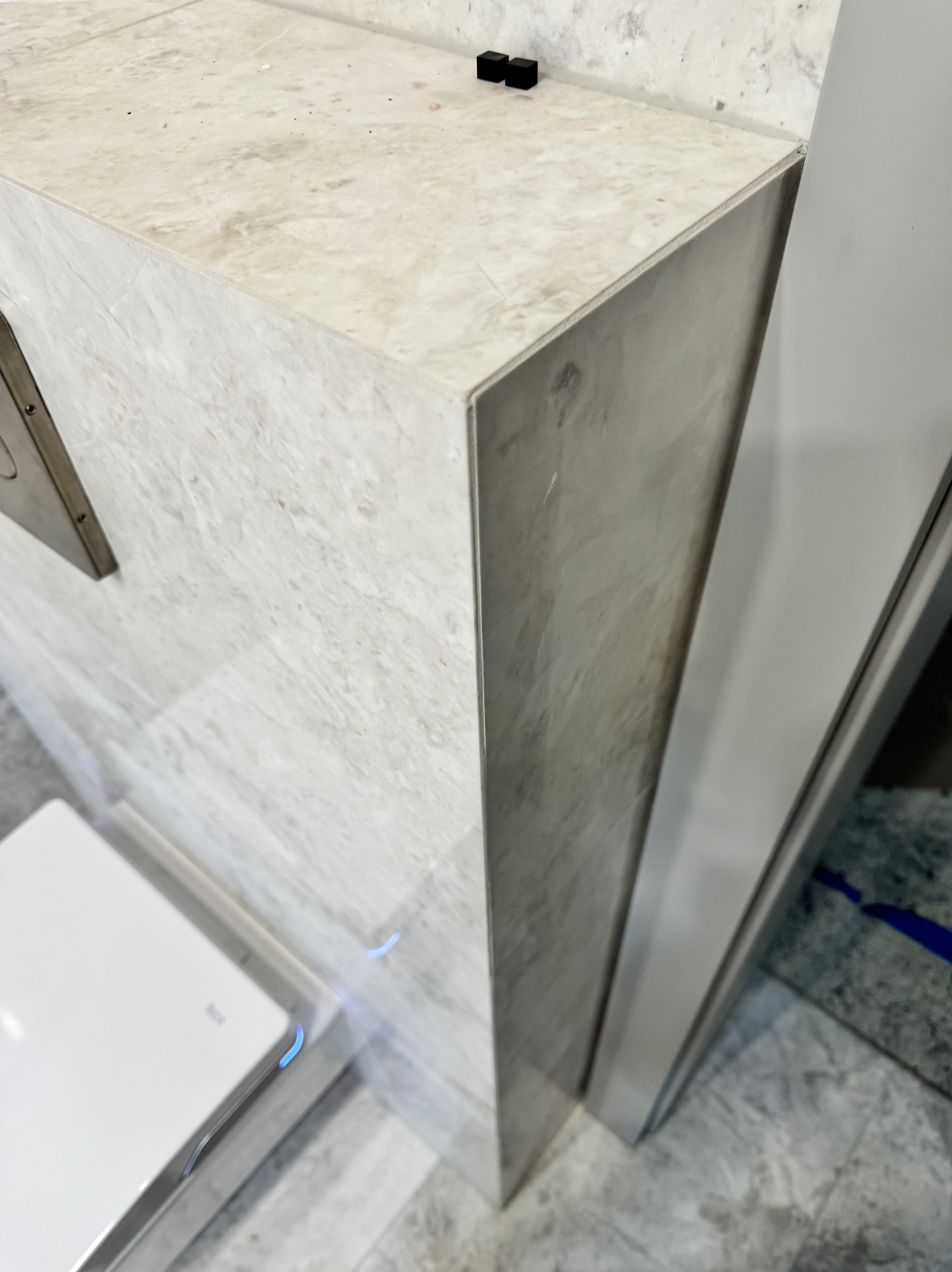 Wykończenie łazienki w Warce: narożnik obłożony marmurowymi płytami, widoczny fragment toalety z podświetleniem LED i czarne akcesoria na blacie.