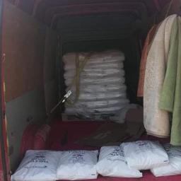 Fast-Trans Przeprowadzki Torun - Wnętrze czerwonego busa załadowane paletą zafoliowanych worków i kilkoma workami z napisem 'TABLETKI SOLNE 25 KG', zabezpieczone pasami transportowymi, z wiszącymi ubraniami po prawej stronie.