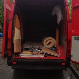 Fast-Trans Przeprowadzki Torun - Otwarty czerwony furgon załadowany meblami i osobistymi rzeczami, widok z tyłu na mokry chodnik.