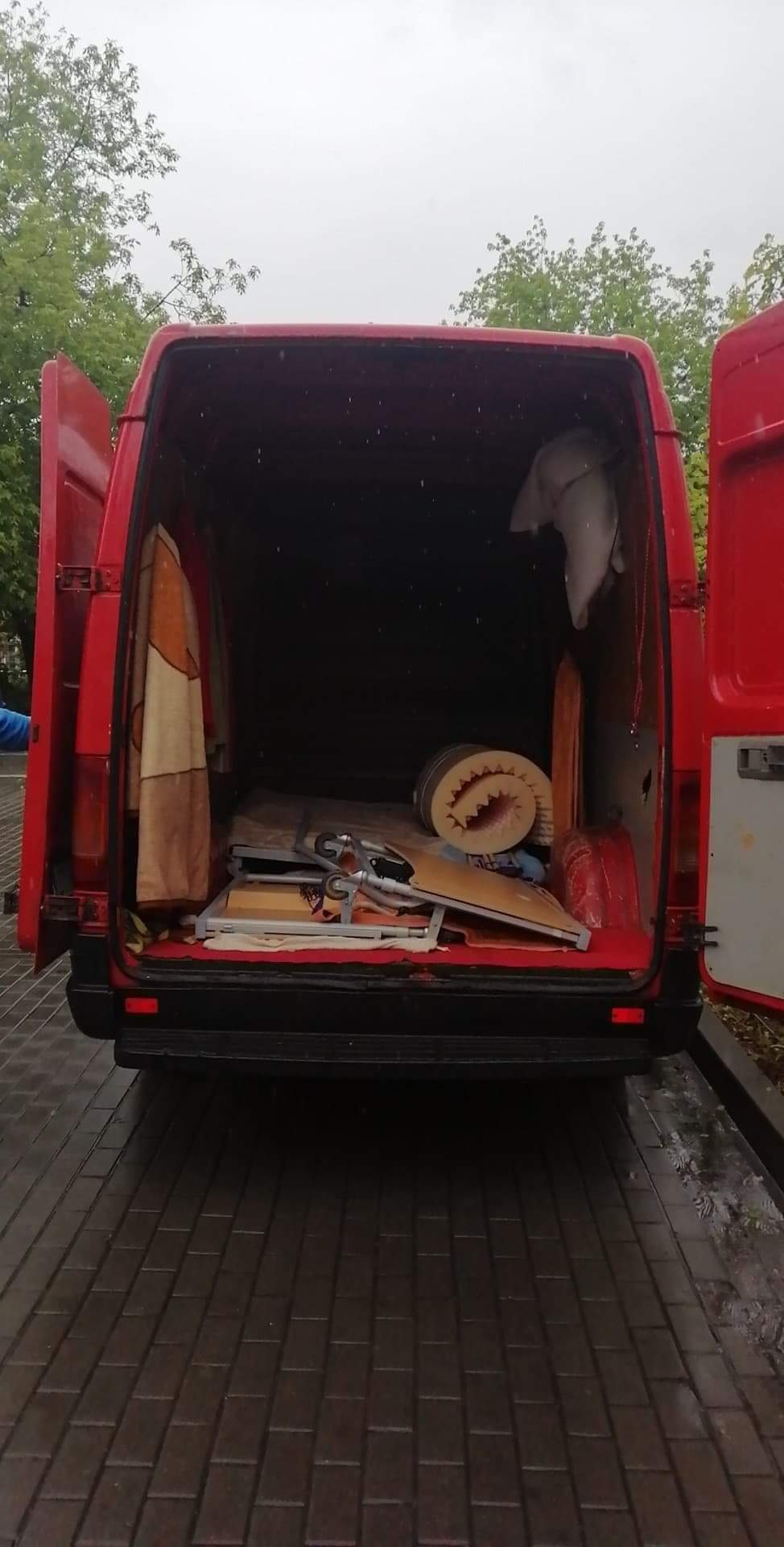 Otwarty czerwony furgon załadowany meblami i osobistymi rzeczami, widok z tyłu na mokry chodnik.