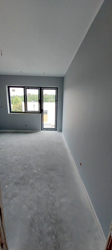 Świeżo pomalowane na szaro wnętrze pokoju z oknem i drzwiami balkonowymi; widoczne ślady farby na podłodze.