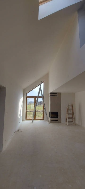 Wnętrze z wysokim sufitem po świeżym pomalowaniu na jasny kolor, z dwoma drabinami ustawionymi w różnych miejscach pomieszczenia, widok na zewnątrz przez okno