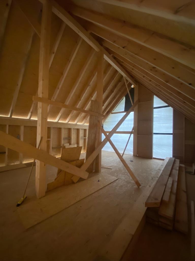 Wnętrze domu szkieletowego w trakcie budowy, widoczne drewniane ramy konstrukcyjne, podłoga z płyt OSB i okno z folią ochronną.