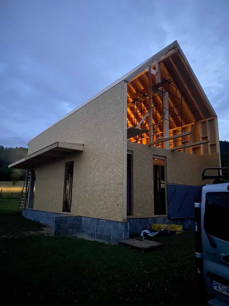 Surowy stan budynku z drewnianą konstrukcją szkieletową i płytami OSB na tle pochmurnego nieba o zmierzchu.