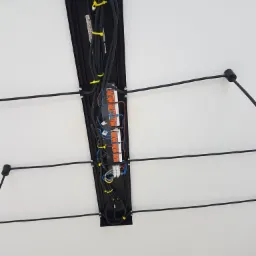 Widok z dołu na podwieszany sufit z widoczną instalacją elektryczną w czarnej obudowie, kable zabezpieczone żółtymi opaskami, widoczne złączki elektryczne.