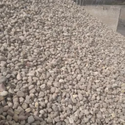 Góra jasnych, okrągłych kamieni różnej wielkości, z betonowymi elementami konstrukcyjnymi w tle.