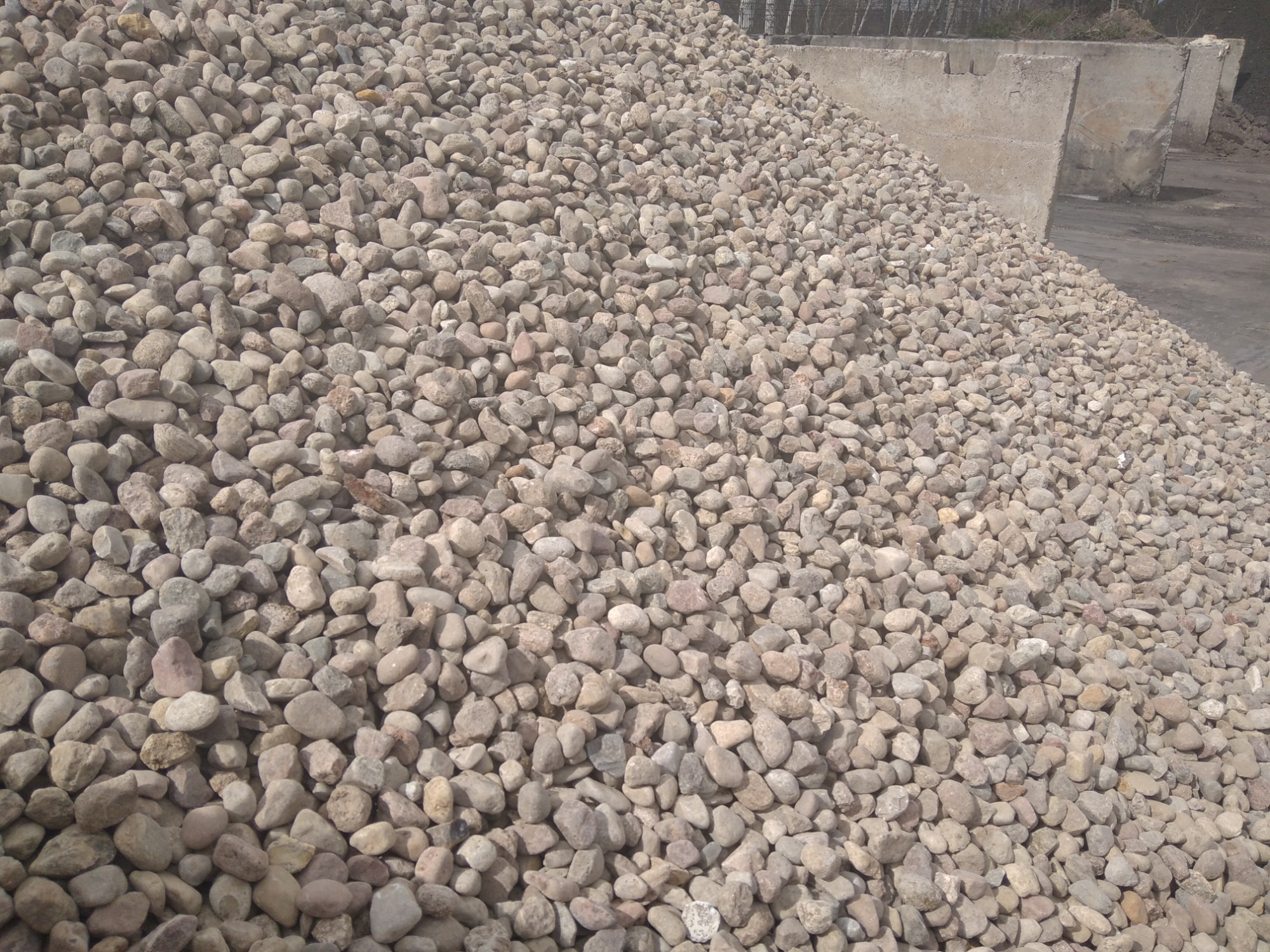 Góra jasnych, okrągłych kamieni różnej wielkości, z betonowymi elementami konstrukcyjnymi w tle.