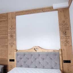 Stanisław Strzęp - Pokój z drewnianą boazerią i ramą łóżka z motywami góralskimi, szara tapicerowana rama łóżka z wycięciem w kształcie serca, biała ściana