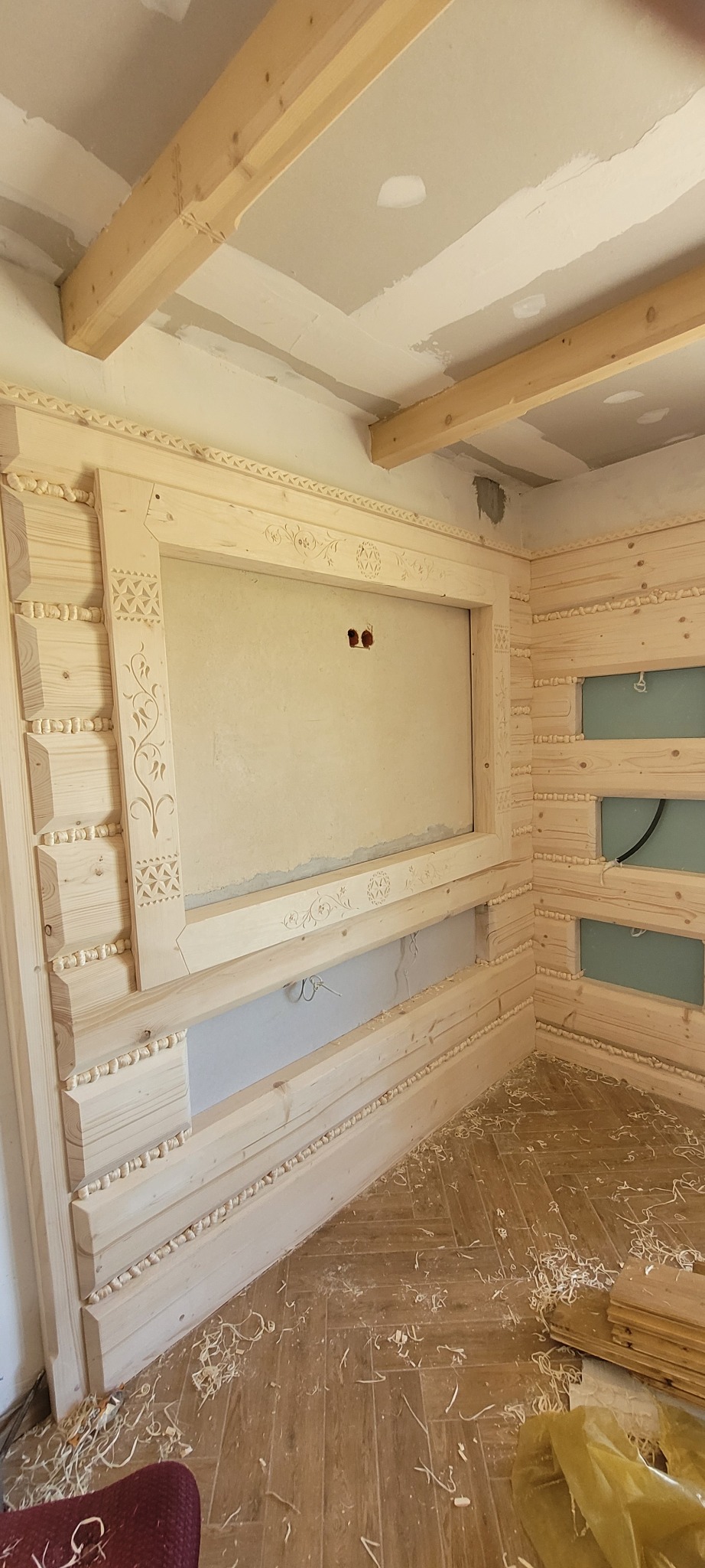 Fragment wnętrza w Bańskiej Wyżnej w trakcie prac wykończeniowych z widoczną drewnianą boazerią zdobioną rzeźbieniami, surowy stan ściany przygotowany pod montaż telewizora oraz drewniane bale...