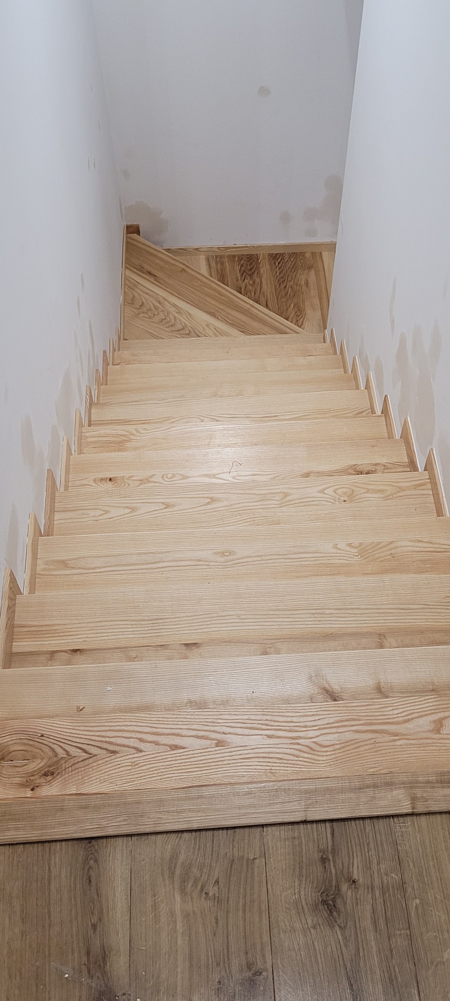 Nowe, jasne schody drewniane z widocznymi śladami po pracach wykończeniowych na ścianach i podłodze.