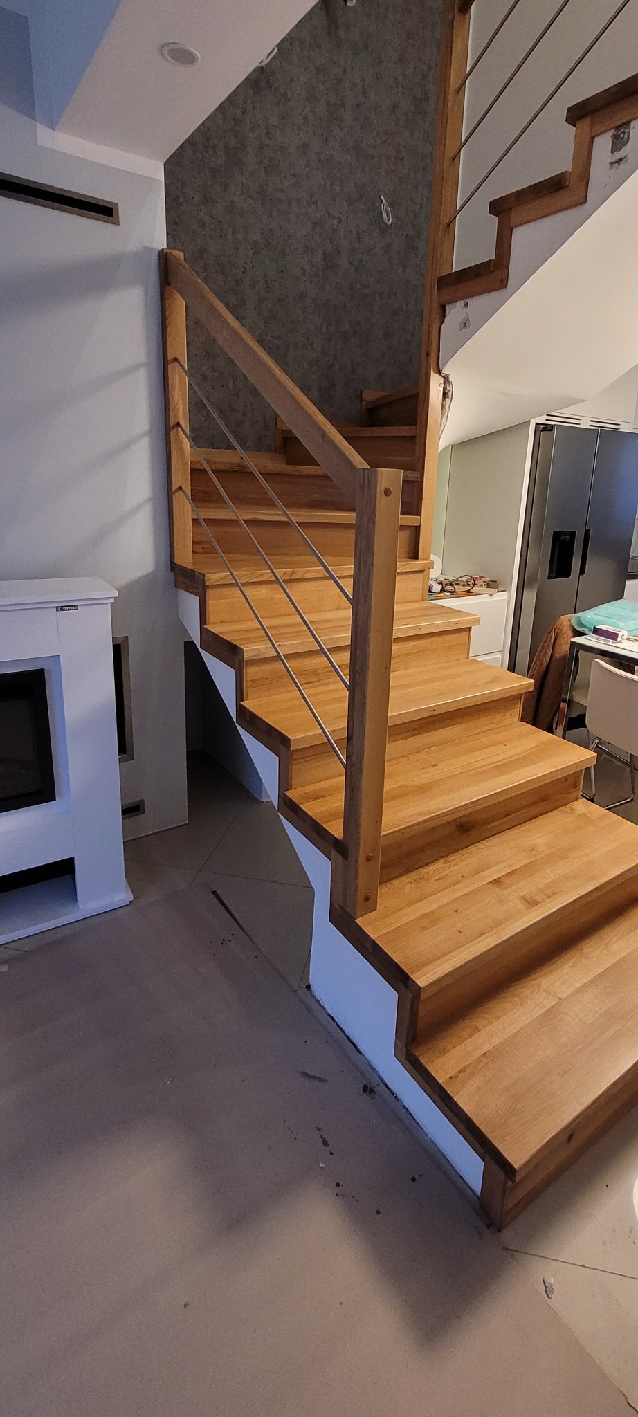 Drewniane schody z metalowymi barierkami, jasne drewno, widok z dołu, minimalistyczny design, biały kominek obok.